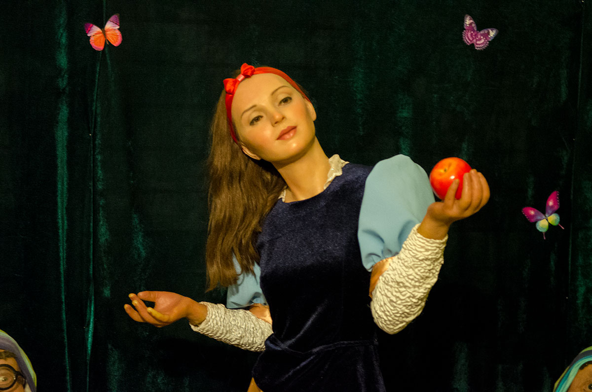 Выставка восковых фигур в Балтийском доме открывается изображением симпатичной девушки с яблоком в руке на фоне занавеса с бабочками.